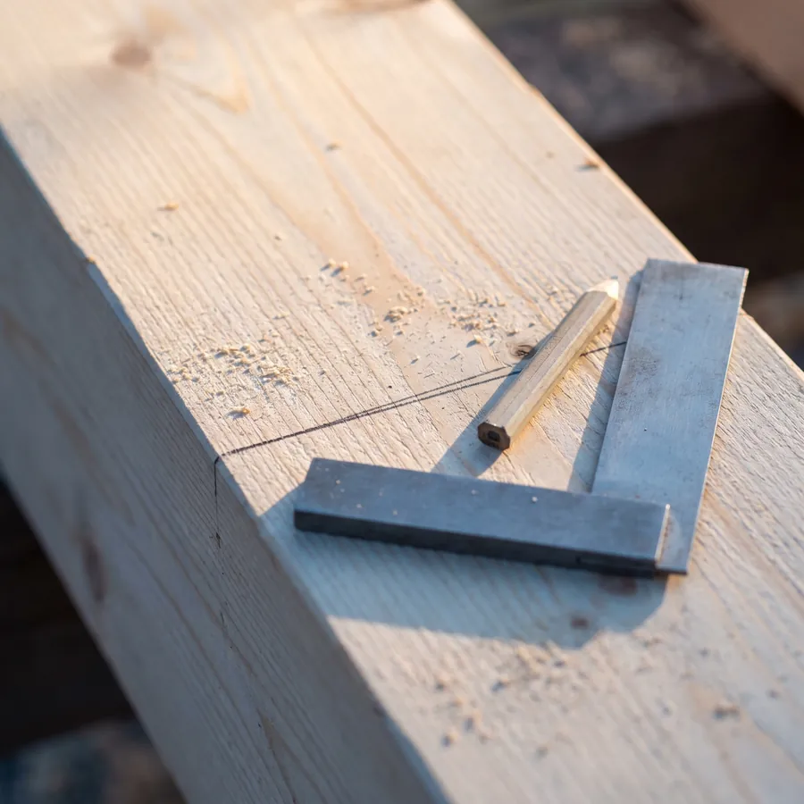Zimmermannswinkel und Bleistift auf einem Balken mit angerissener Linie